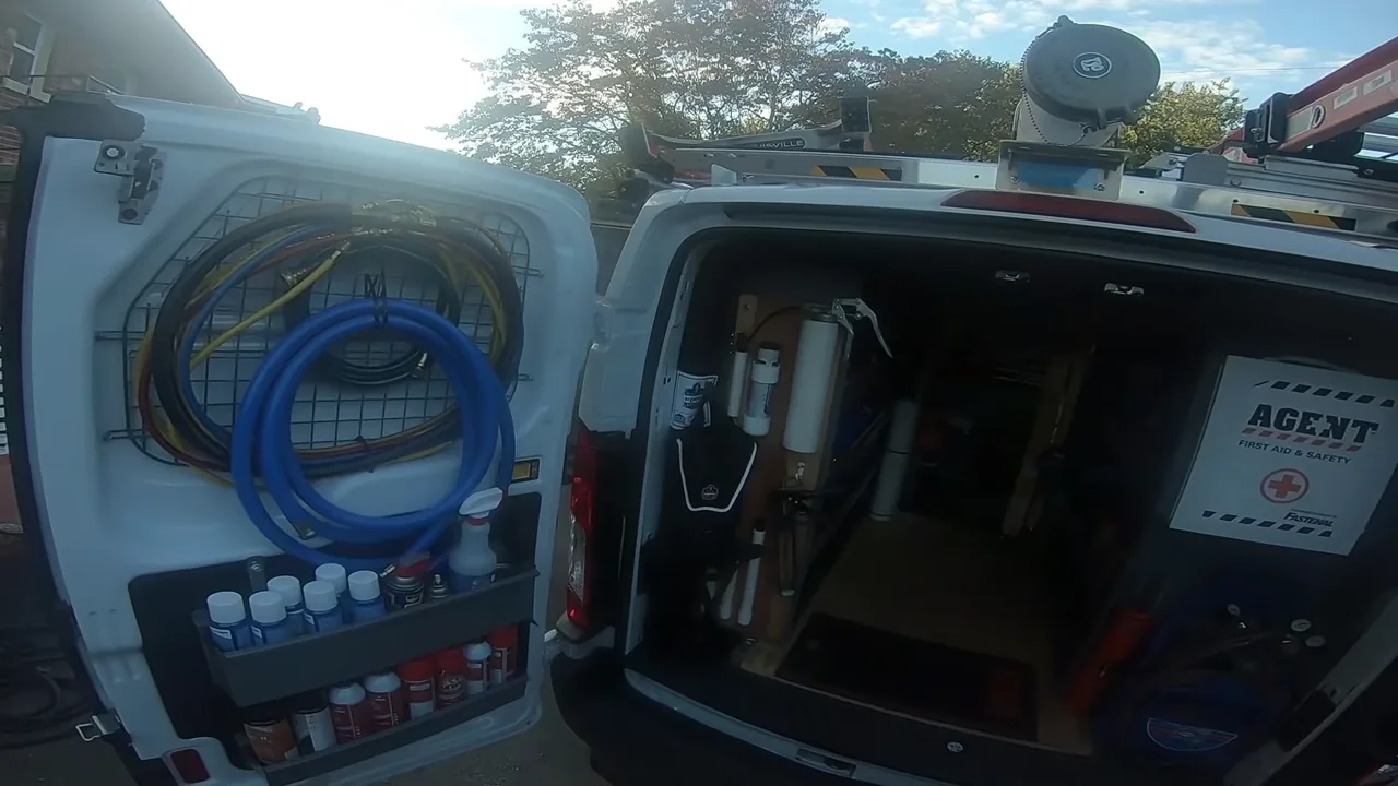 Rear doors of a white service van open to show coiled gauge hoses and supplies on one door and organized tool storage inside